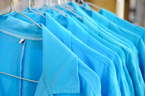 A row of freshly laundered blue uniforms hangs neatly on metal hangers, showcasing crisp collars and smooth fabric.
